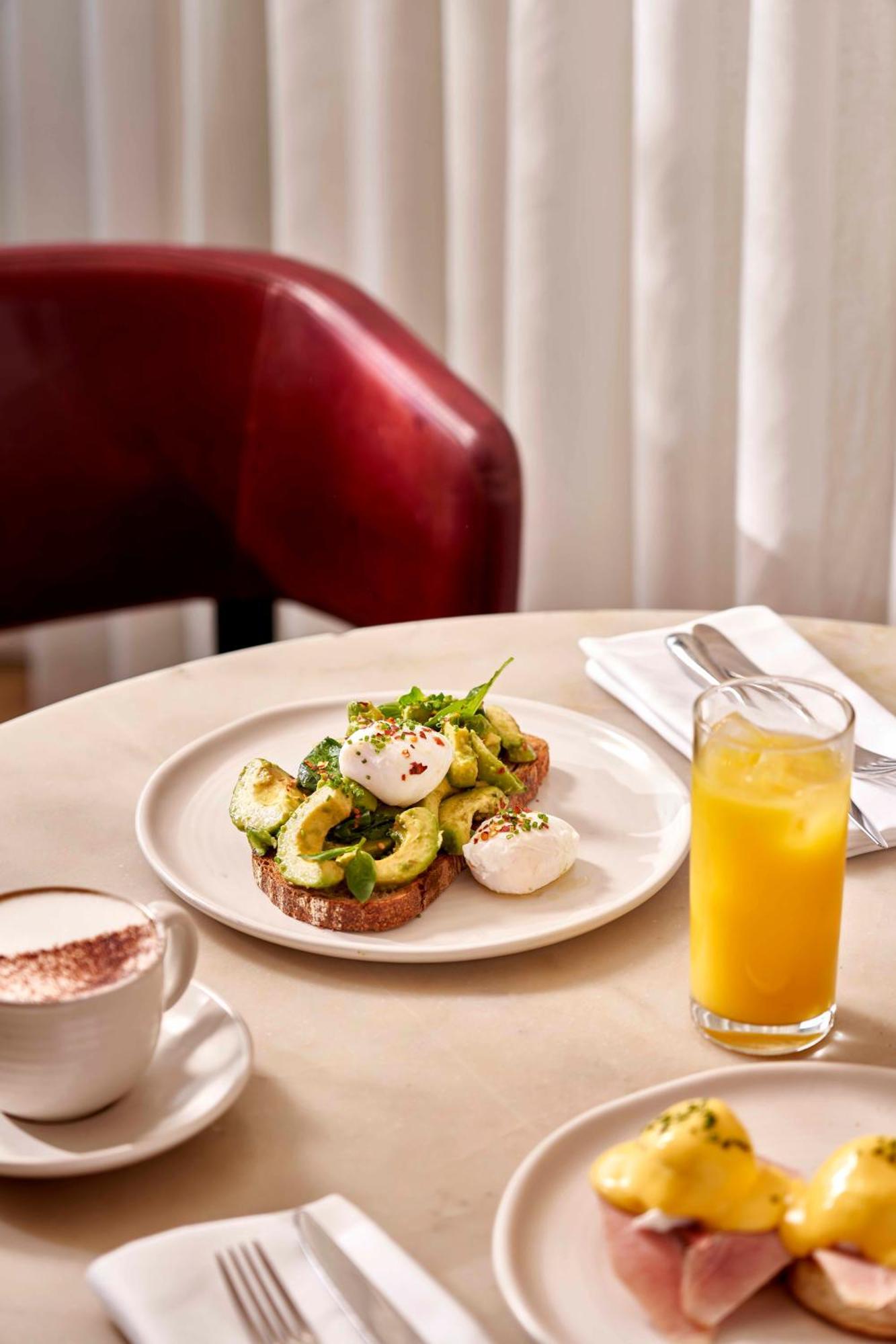 Sea Containers London Hotell Eksteriør bilde The photo shows a plate of food featuring sliced avocado on toast, topped with poached eggs and garnished with herbs and spices. The toast appears to be whole grain. There's also a glass of orange juice on the side and a cup of coffee, possibly cappu