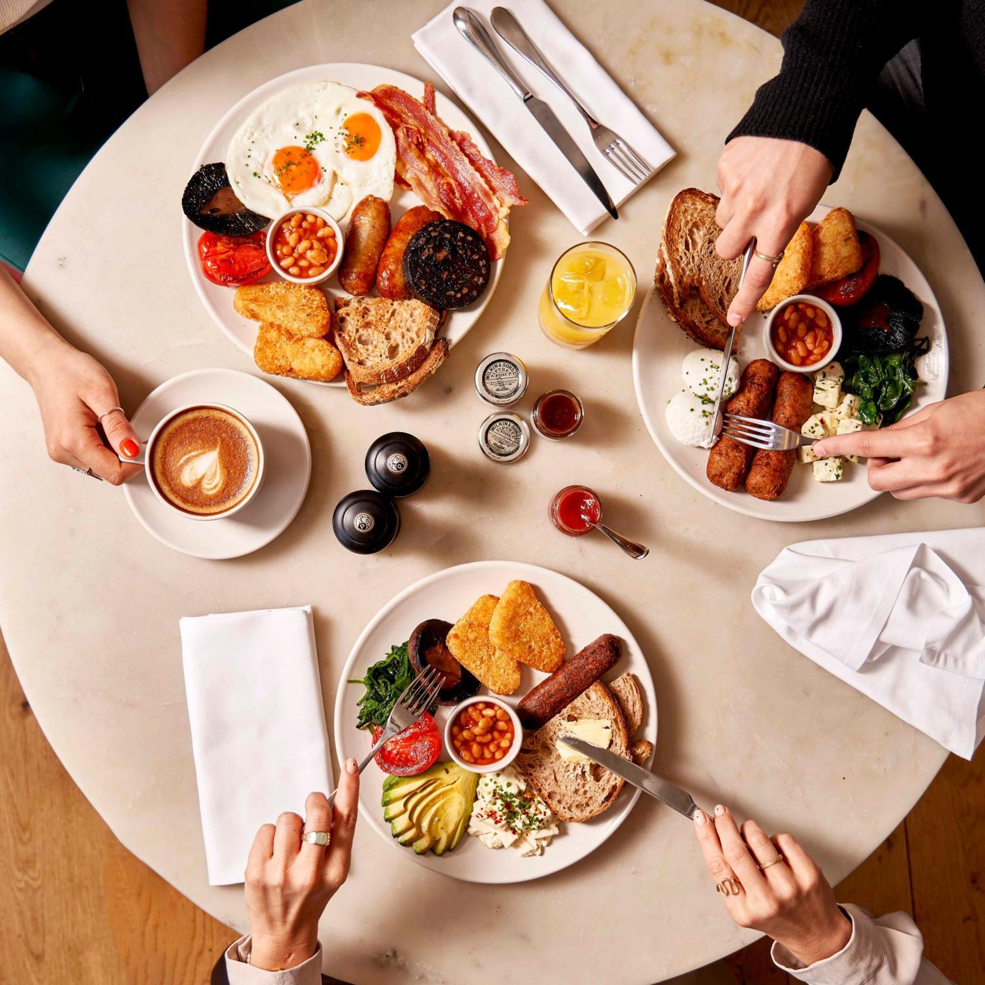 Sea Containers London Hotell Eksteriør bilde The photo shows a beautifully set table with three plates of food, each featuring a variety of breakfast items. The dishes include:

1. **Main Plates**: Each plate contains a hearty breakfast spread, which includes items like eggs, bacon, sausages, b