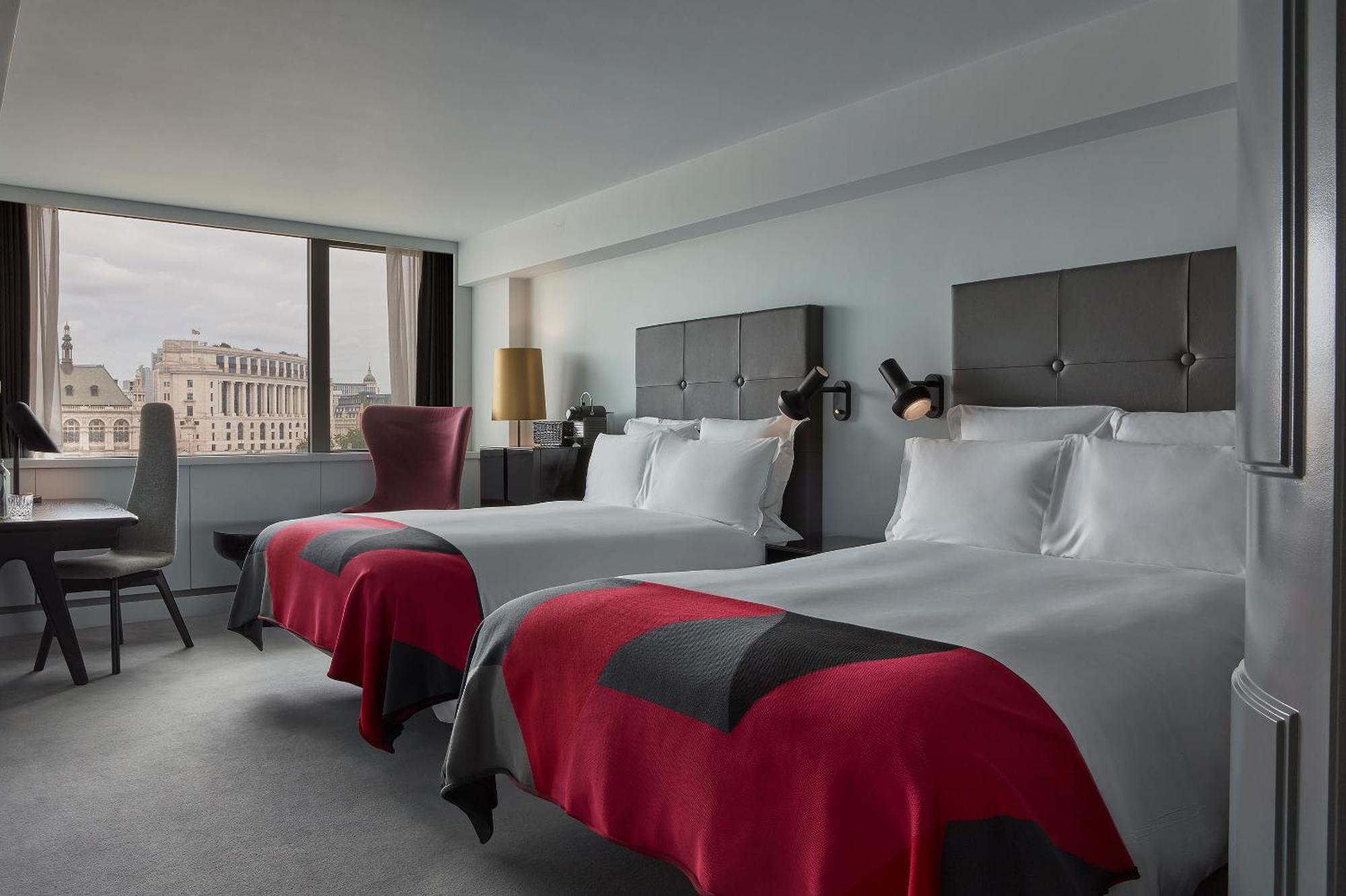 Sea Containers London Hotell Eksteriør bilde The photo displays a modern hotel room featuring two beds with stylish bedspreads in red and gray. The walls are painted in a soft light color, and there are bedside lamps affixed to the headboards. A chair is positioned by a large window that offers