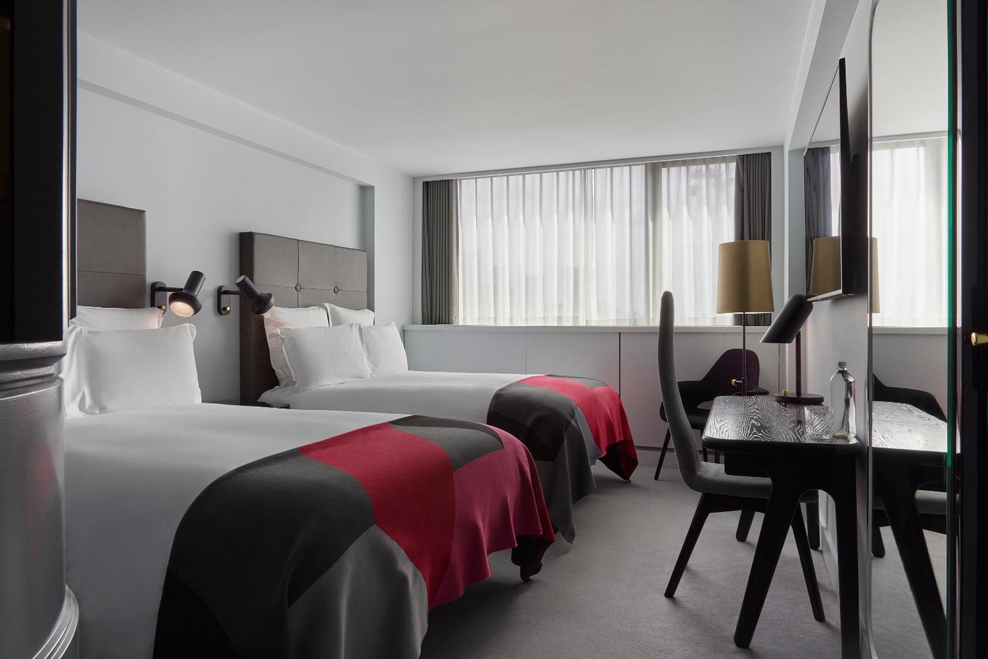 Sea Containers London Hotell Eksteriør bilde The photo shows a hotel room featuring two twin beds with stylish dark headboards and bed linens that have a red and gray design. There are bright white pillows on the beds, and the room has a modern, minimalist aesthetic. Large windows with sheer dr