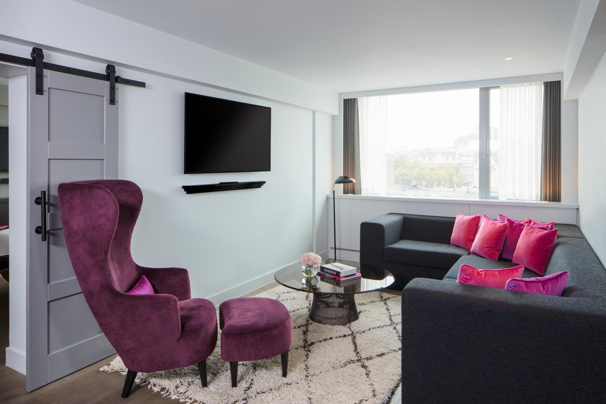 Sea Containers London Hotell Eksteriør bilde The photo shows a modern living room with a clean and stylish design. There is a large window that allows natural light to fill the space. A comfortable dark sofa is accompanied by vibrant pink cushions, adding a pop of color. Next to the sofa is a r