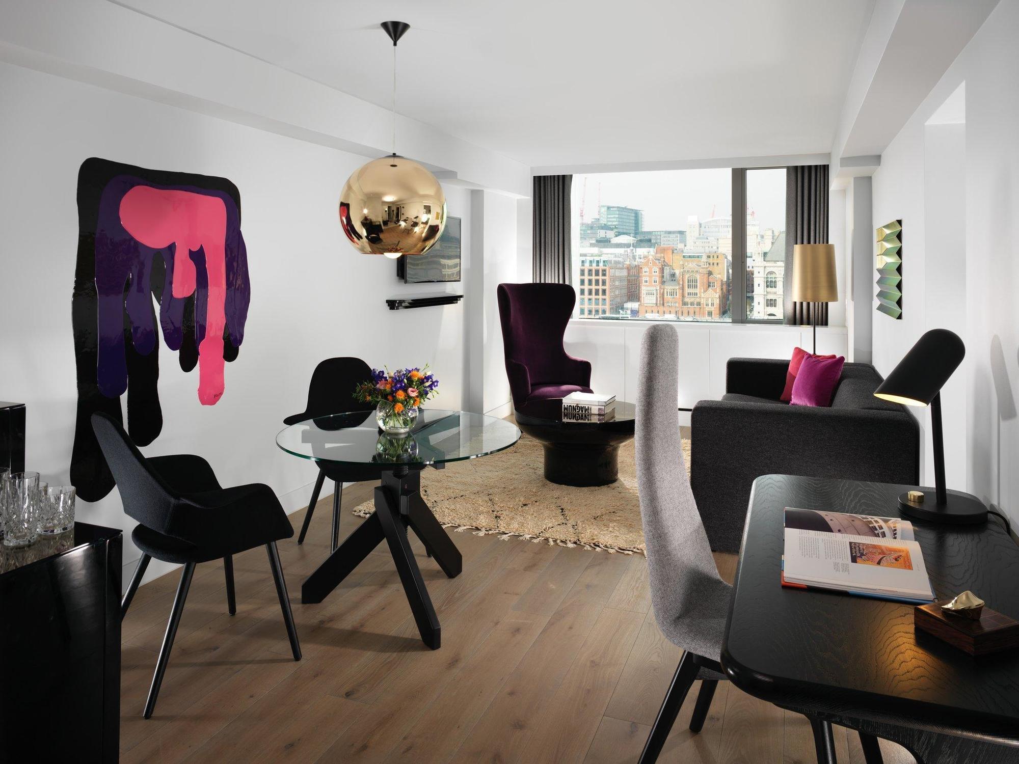 Sea Containers London Hotell Eksteriør bilde The photo shows a modern and stylish living space. It features a light-colored wooden floor and a layout that includes a glass dining table surrounded by black chairs. There’s a lounge area with a couple of armchairs, one of which has a playful and u