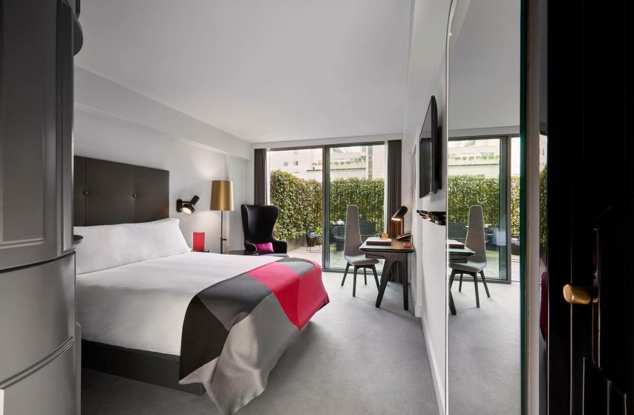 Sea Containers London Hotell Eksteriør bilde The photo shows a modern hotel room featuring a large bed with a minimalist design. The bed is adorned with a colorful bedspread, primarily in shades of gray, white, and pink. There are two large windows that provide natural light and overlook a gree