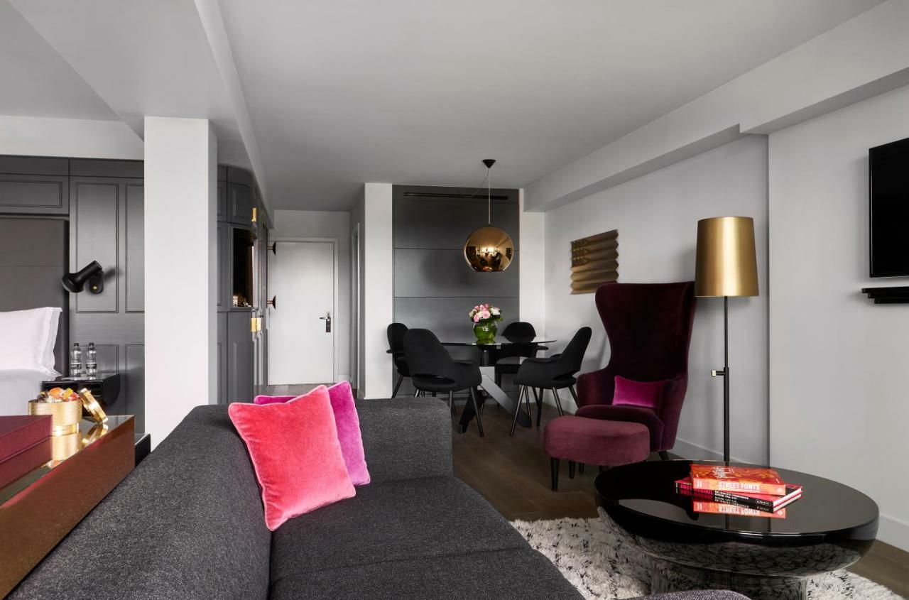 Sea Containers London Hotell Eksteriør bilde The photo shows a modern and stylish living space. There is a gray sofa with two pink cushions in the foreground. In the background, there is a dining area with a round black table and black chairs. A decorative pendant light hangs above the table. T